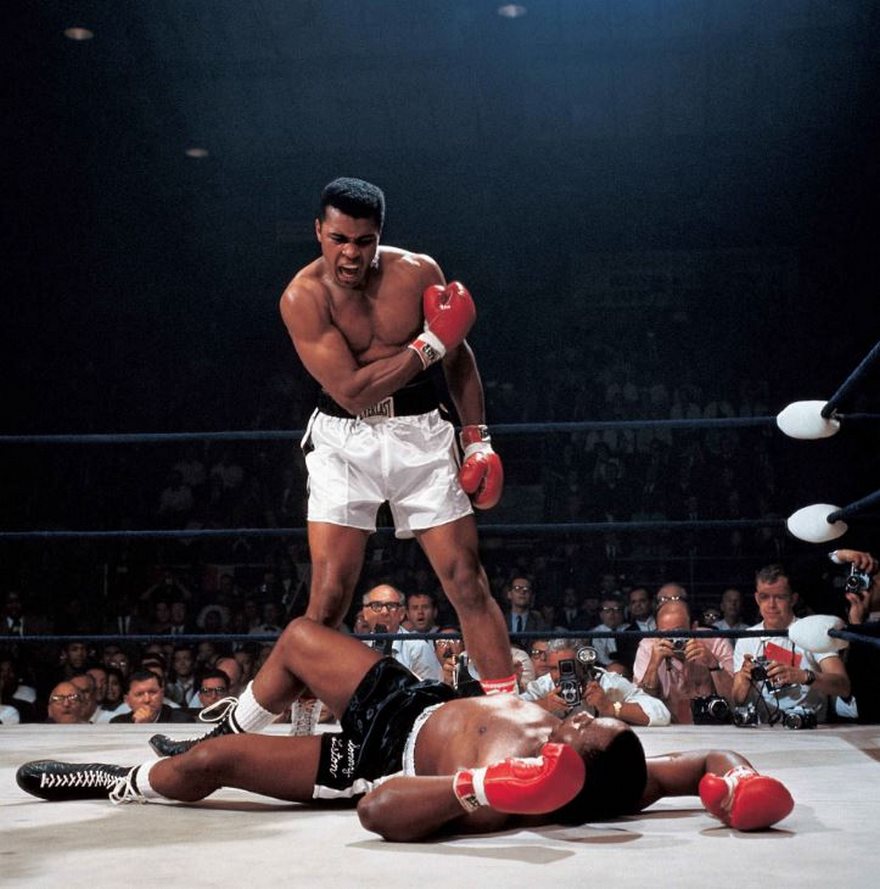 Boxing legend standing triumphant over fallen opponent in one of history's most famous photos.