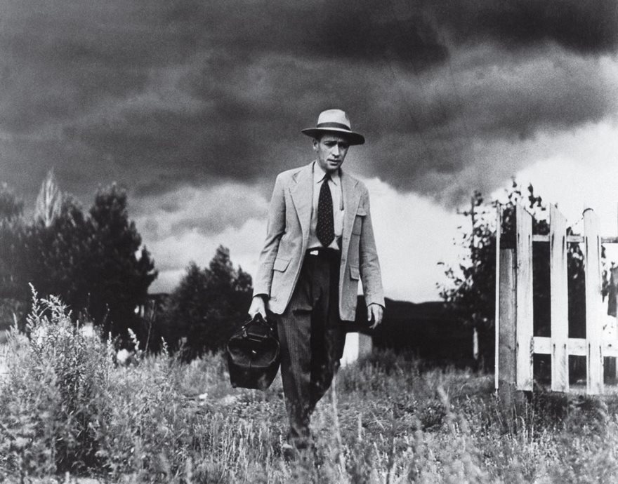 A man in a suit and hat carrying a briefcase, walking through a field under a stormy sky, representing famous historical photo.