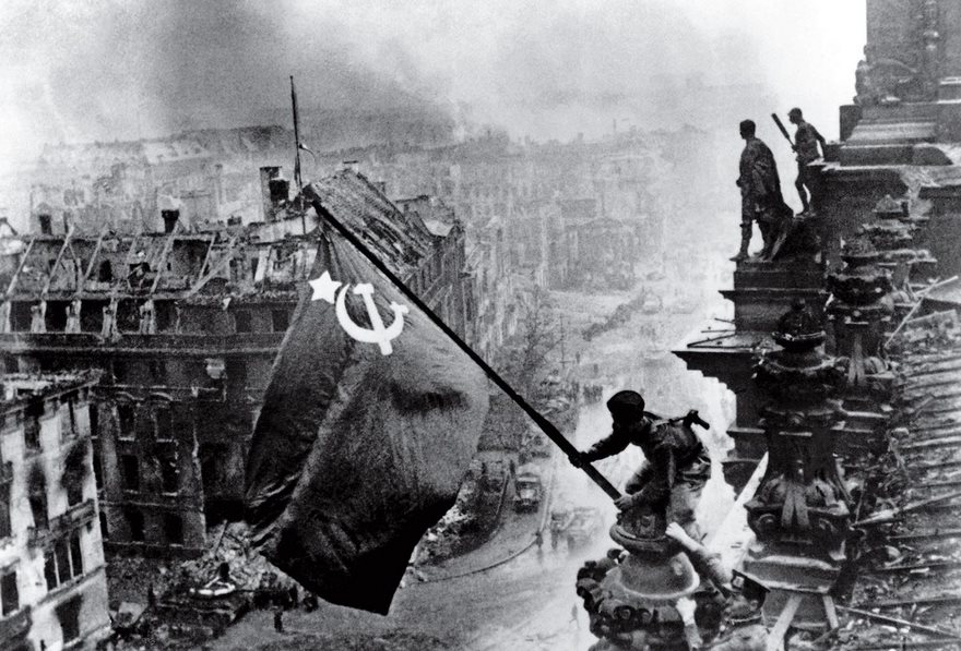Soldier raising Soviet flag over Berlin during WWII, capturing a historic moment in photography.