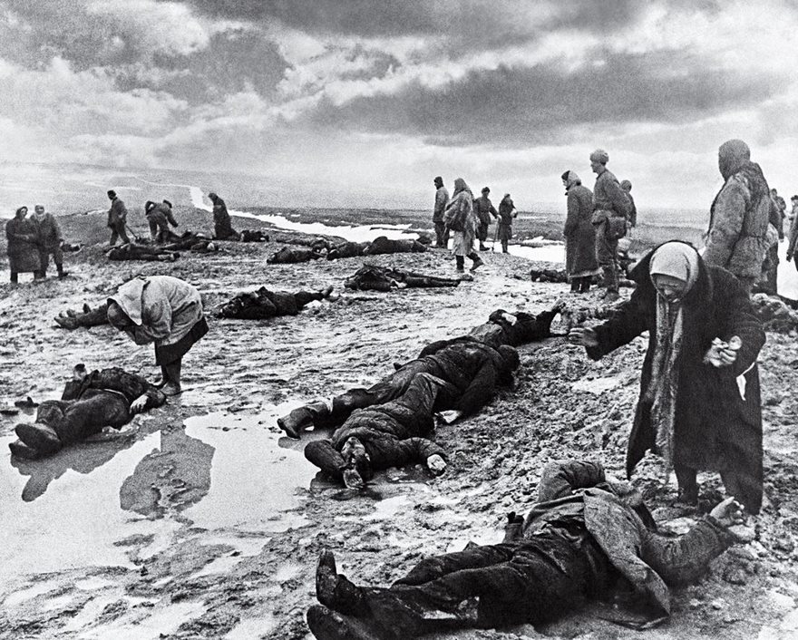Historical photo showing people standing and lying on a battlefield, reflecting the somber aftermath of conflict.