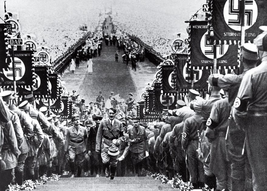A historical photo showing a large group of men in uniform with N**i symbols during a notable event in history.
