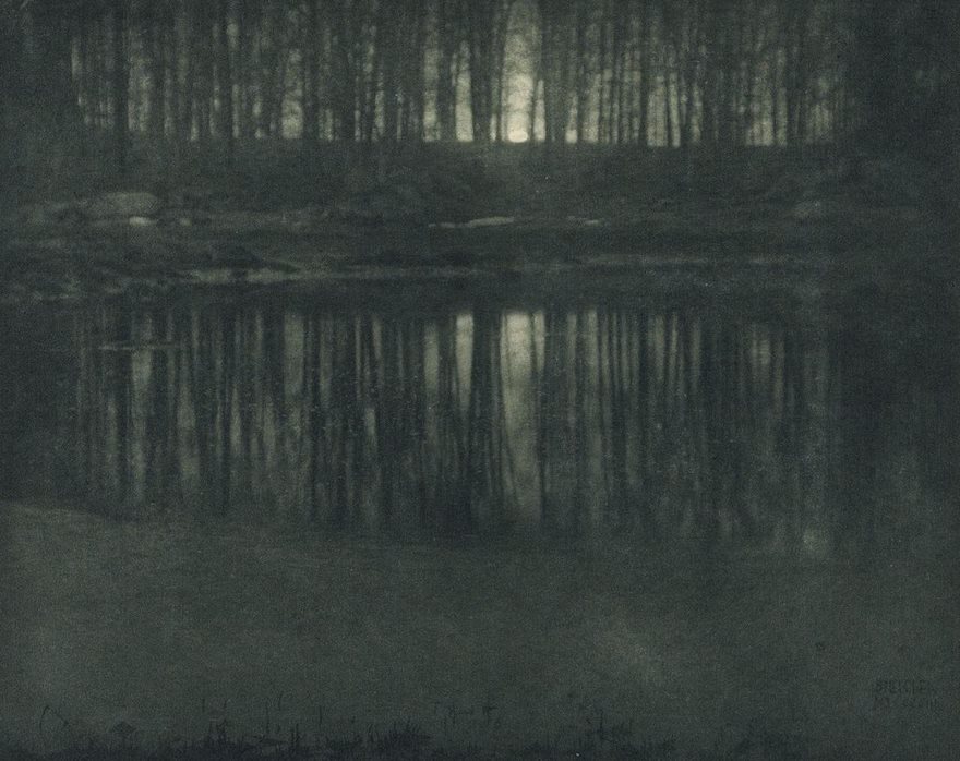 Famous historical photo of a serene lake reflecting a moonlit forest at night.