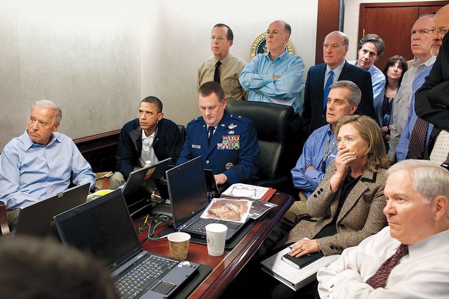 Famous historical photo of a group intently watching a monitor in a conference room, including military and civilian officials.