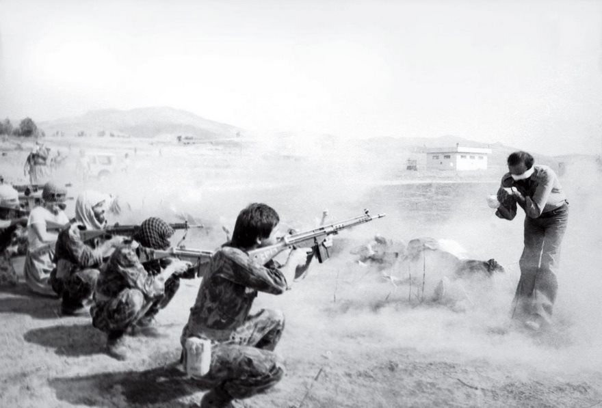 Soldiers aiming rifles at a blindfolded man, historic photo scene enveloped in smoke.