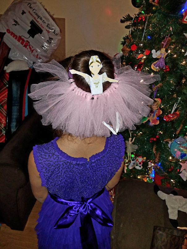 Creative Christmas hairstyle featuring a ballerina design with a tutu hair accessory near a decorated tree.