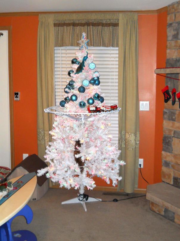 A Christmas tree creatively protected from pets, cut halfway with ornaments on top, and a train running around the middle.
