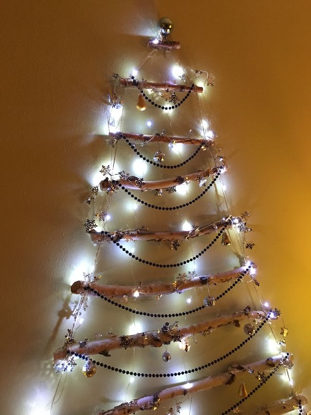 Wall-mounted Christmas tree made of decorated sticks and lights, a genius way to protect from cats and dogs.