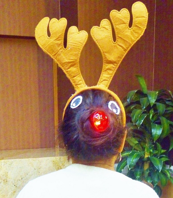 Creative Christmas hairstyle with reindeer antlers and a shiny nose accessory on hair bun.