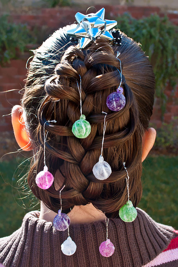 Creative Christmas hairstyle with ornate braid adorned with colorful baubles and a blue ribbon on top.