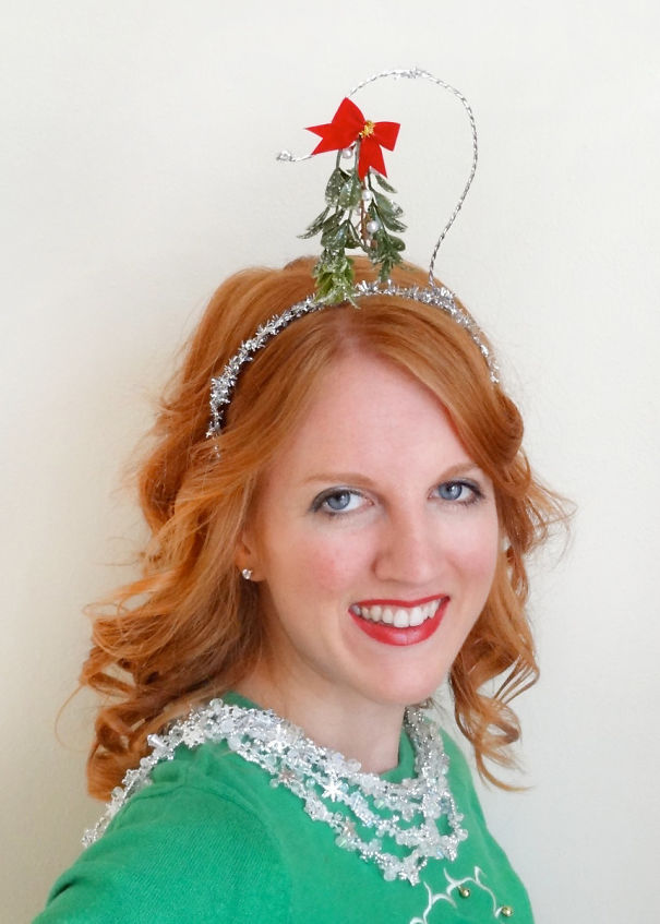 Woman with red hair styled creatively with Christmas decorations, including a headband with festive ornaments.