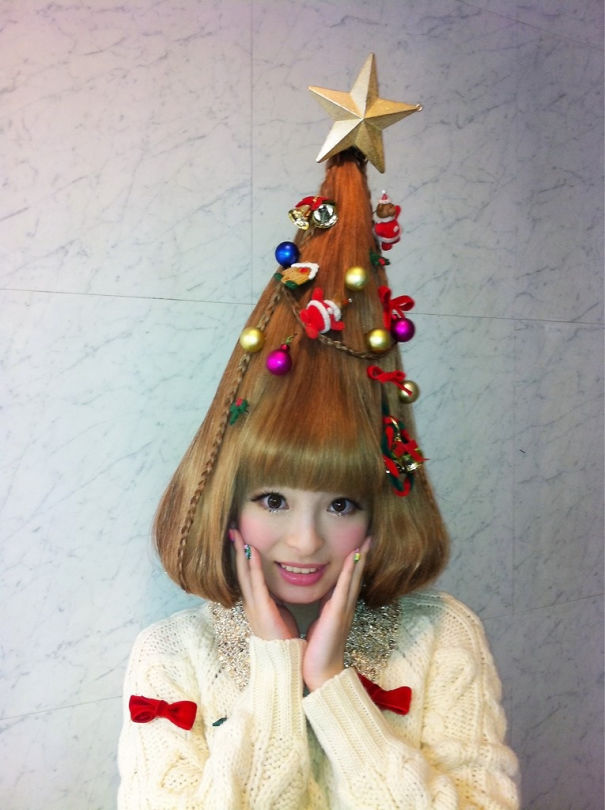 Creative Christmas hairstyle shaped like a tree, decorated with ornaments and a star, worn by a smiling woman.