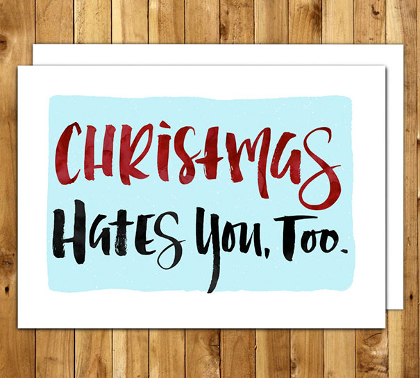 Rude Christmas card with text "Christmas Hates You, Too" on a wooden background.