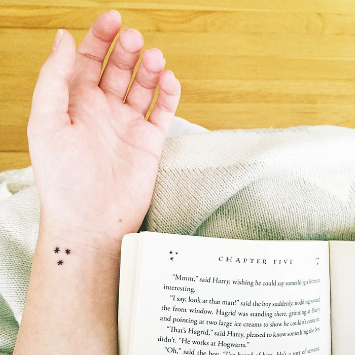 Subtle Harry Potter tattoo of stars on a wrist, shown above an open book.
