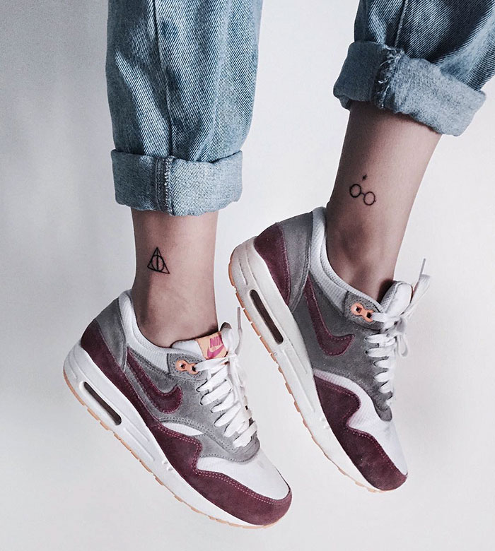 Close-up of subtle Harry Potter tattoos on ankles, featuring symbols, with wearer in rolled-up jeans and Nike sneakers.