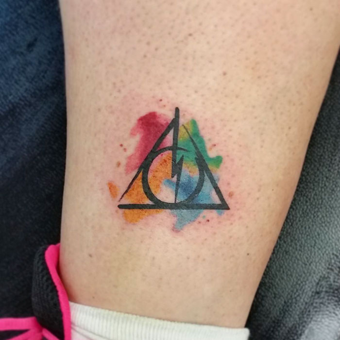 Subtle Harry Potter tattoo with Deathly Hallows symbol over a colorful watercolor background on skin.