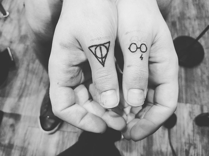 Subtle Harry Potter tattoos on fingers, featuring the Deathly Hallows symbol and Harry's glasses with a lightning bolt.