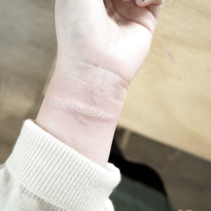 Subtle Harry Potter tattoo of "Dumbledore's Army" in white ink on a wrist.