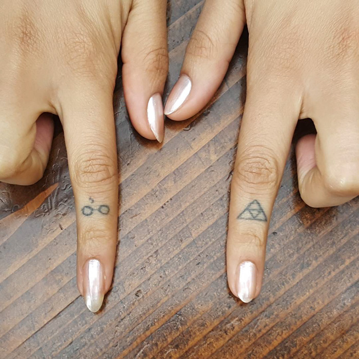 Two subtle Harry Potter tattoos on fingers, featuring glasses and a triangle.