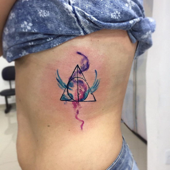 Subtle Harry Potter tattoo of Deathly Hallows design with watercolor effect on a person's side.