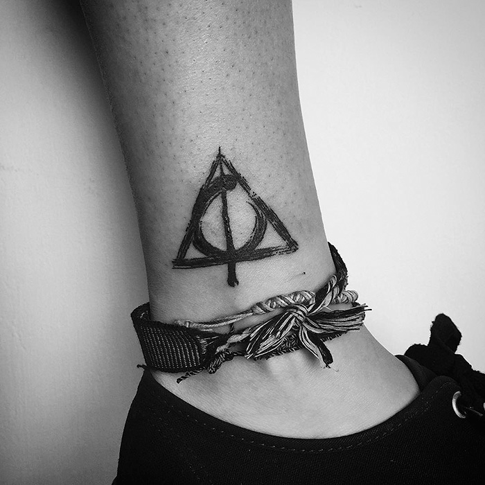Subtle Harry Potter tattoo of the Deathly Hallows on an ankle, next to a braided anklet.