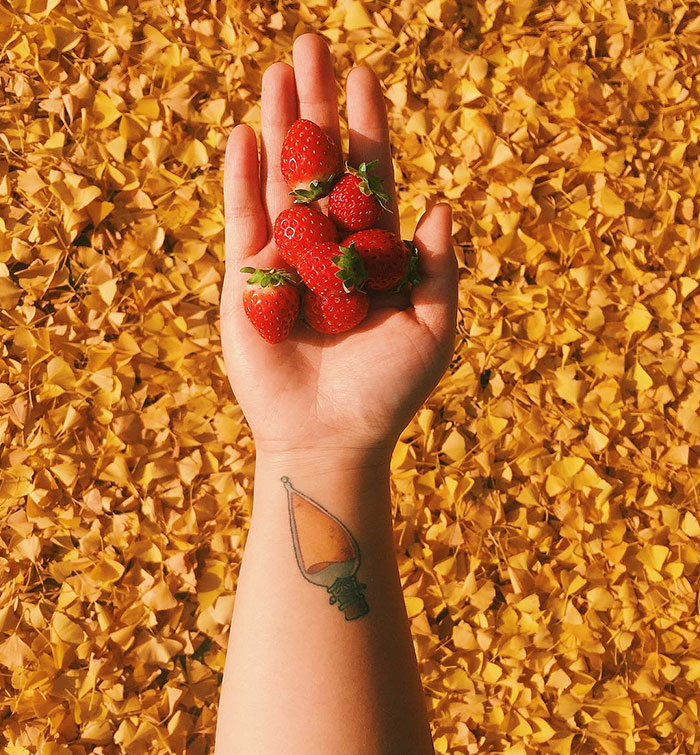 Hand holding strawberries with a subtle Harry Potter tattoo on wrist against a background of yellow leaves.