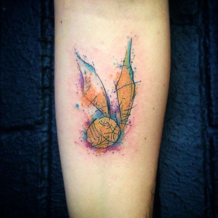 Colorful Golden Snitch tattoo on forearm, a subtle Harry Potter design for true fans.