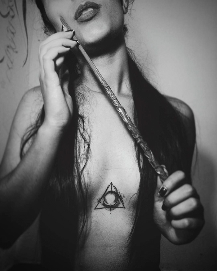 Woman with Deathly Hallows tattoo and wand, a subtle Harry Potter symbol.