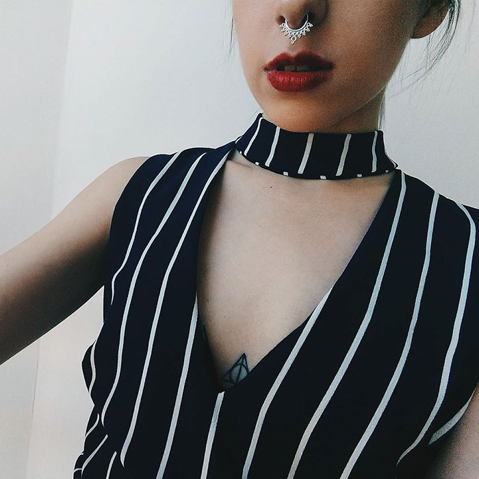 Close-up of a subtle Harry Potter tattoo featuring the Deathly Hallows symbol under a striped top.