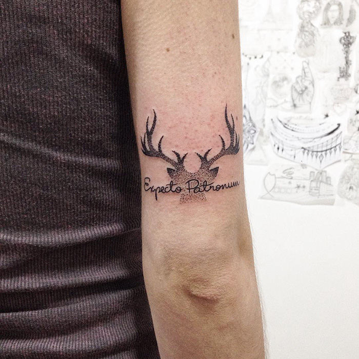 Subtle Harry Potter tattoo featuring "Expecto Patronum" script with antlers on arm.