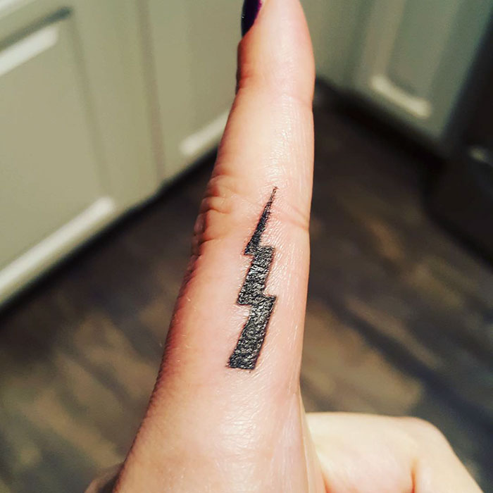 Small black lightning bolt tattoo on a finger, inspired by Harry Potter.