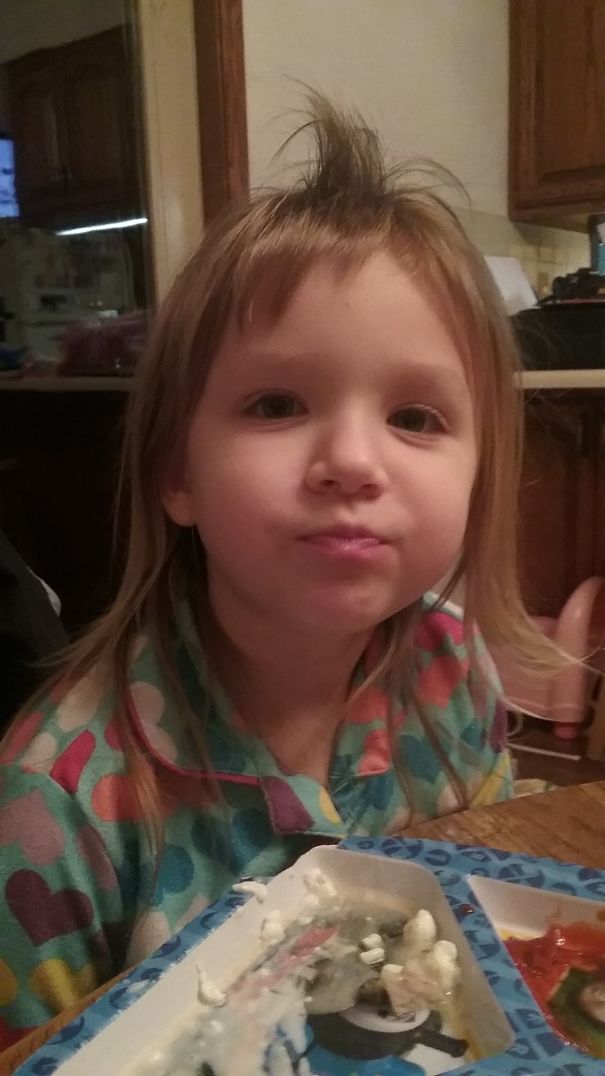 Toddler with a self-cut hairstyle sits at a table, wearing a colorful heart-patterned pajama top.