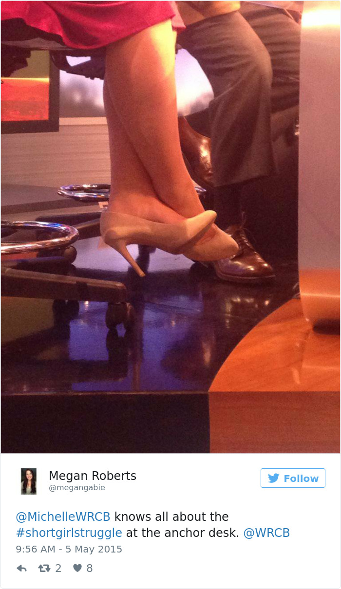 Short person wearing high heels, legs crossed at an anchor desk, highlighting the struggles of reaching high places.