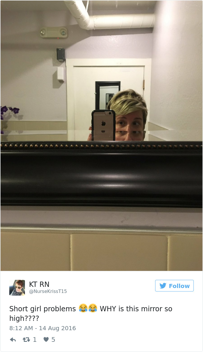 A person holding a phone snaps a selfie, struggling to see over a high bathroom mirror, illustrating short people problems.