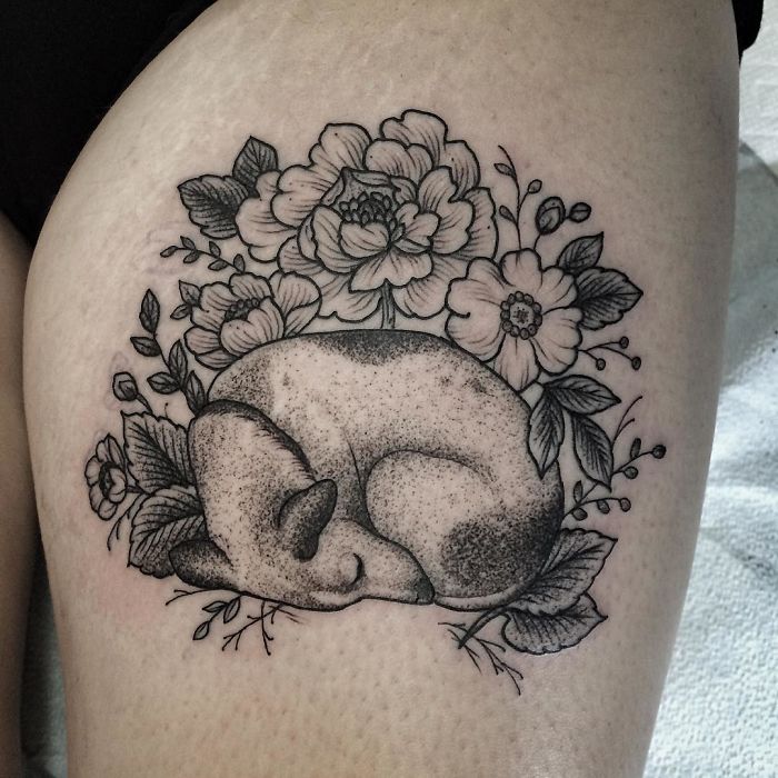 Dog tattoo featuring a sleeping dog surrounded by detailed flowers on skin.