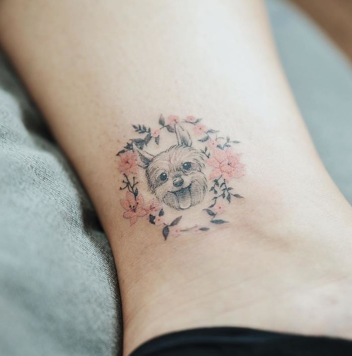 Cute dog tattoo surrounded by pink flowers on skin, showcasing creative dog tattoo ideas.