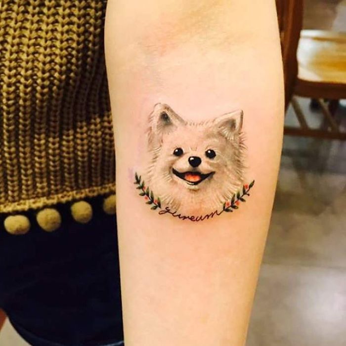 Dog tattoo of a smiling fluffy canine with floral accents on arm.