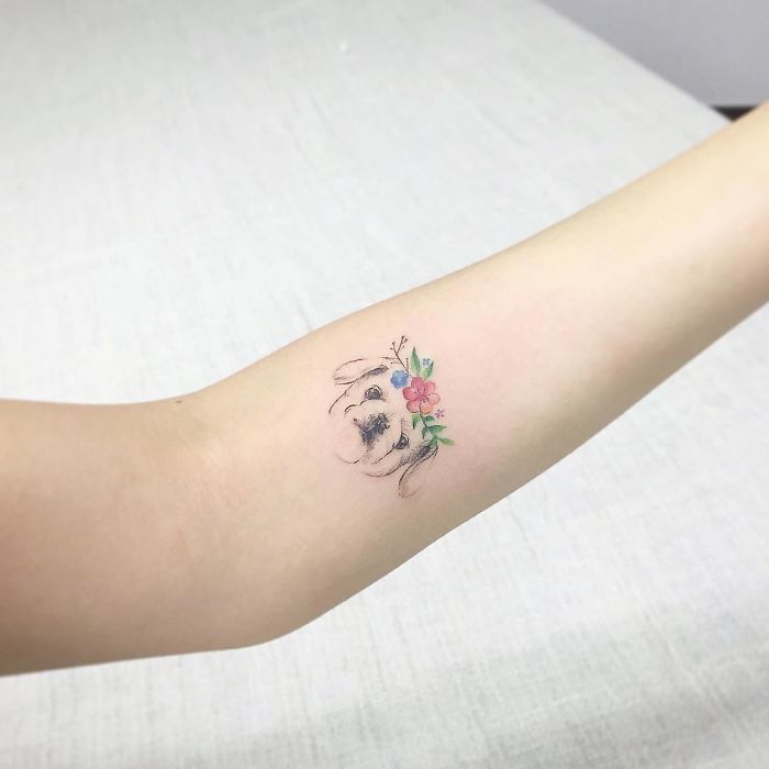 Minimalist dog tattoo with a floral crown on an arm, showcasing creative ink design ideas.