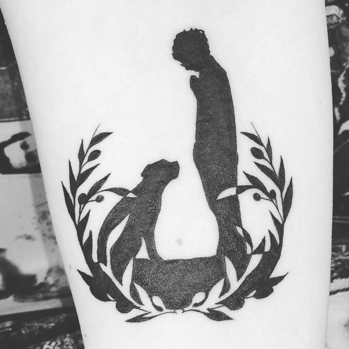 Silhouette dog tattoo featuring a person with laurel wreath design.