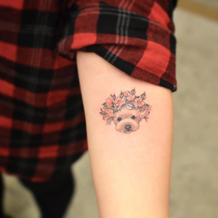 Dog tattoo with floral accents on forearm, person wearing a red plaid shirt.