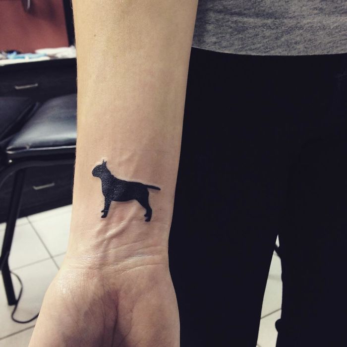 Minimalist dog tattoo on inner wrist, showcasing simple silhouette design.