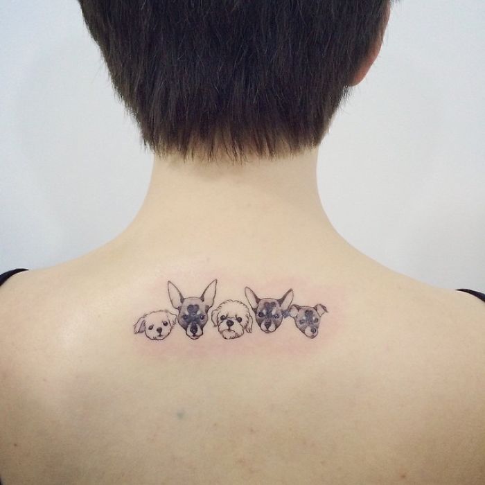 Dog tattoo on upper back featuring five small dog faces in a minimalistic style.