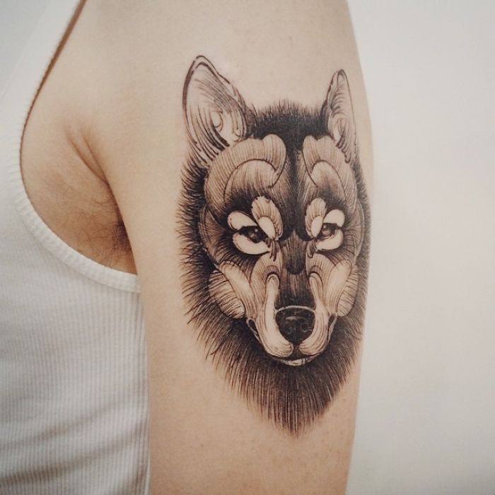 Dog tattoo design with intricate wolf face on upper arm in black ink.