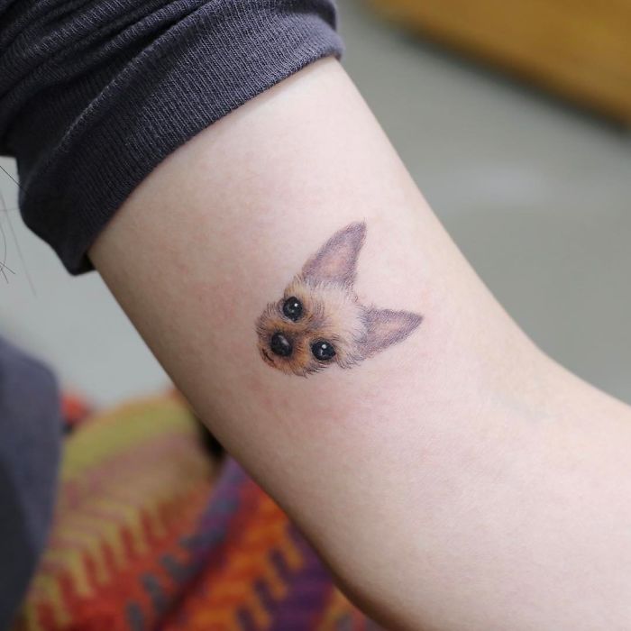 Small dog tattoo on arm, showcasing a detailed and realistic design.
