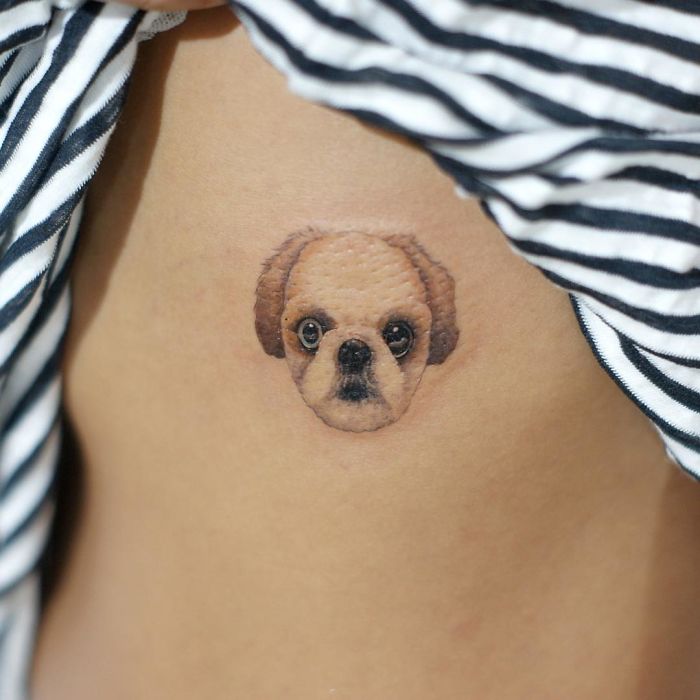 Small dog tattoo on skin under a striped fabric, showcasing a realistic dog face design.