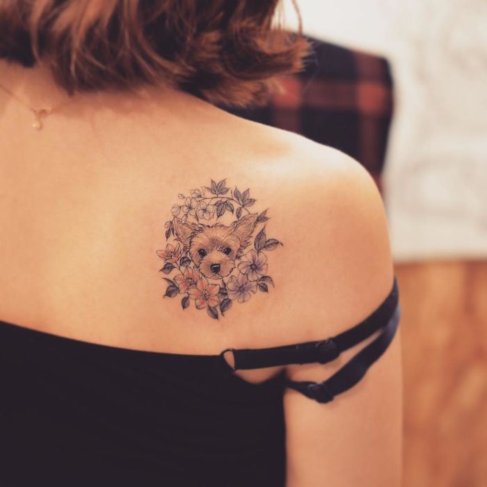 Dog tattoo on shoulder, featuring a cute dog face surrounded by flowers.