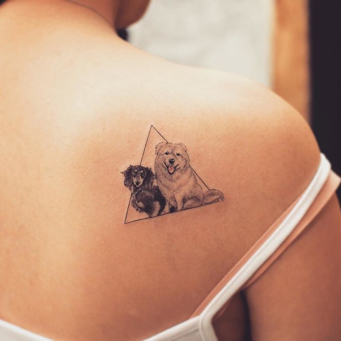 Dog tattoo featuring two dogs inside a triangle on a person's shoulder.