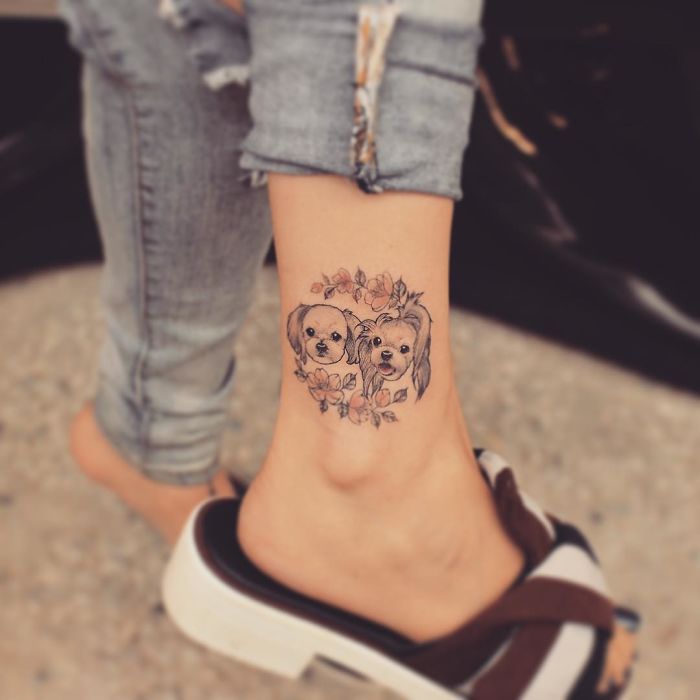 Dog tattoo on ankle featuring two dogs with floral accents, showcasing unique tattoo design ideas.