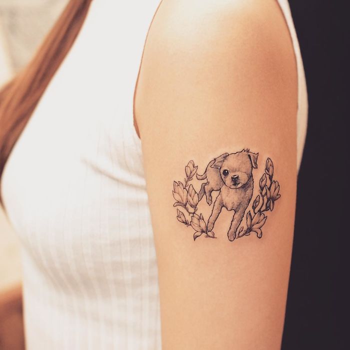 Dog tattoo on a person's arm surrounded by floral design, showcasing cute puppy artwork.