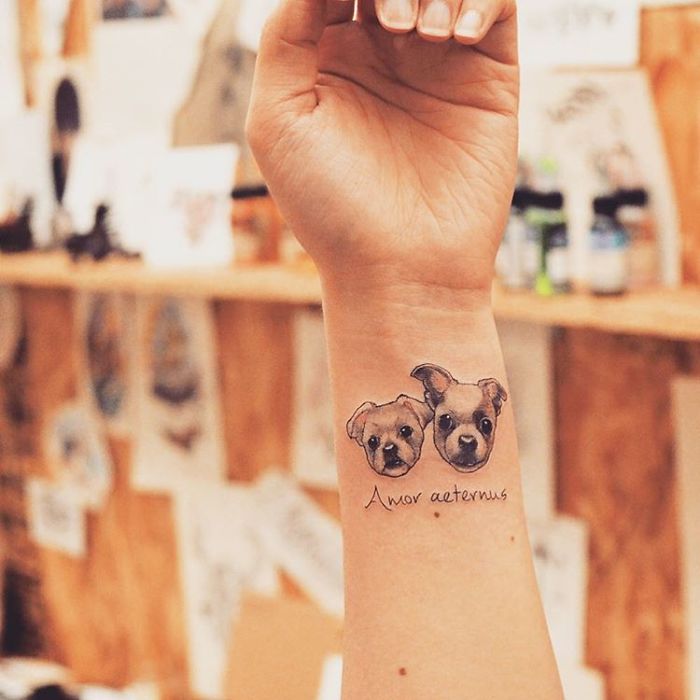 Dog tattoo idea depicting two puppy faces with "Amor aeternus" on a wrist.