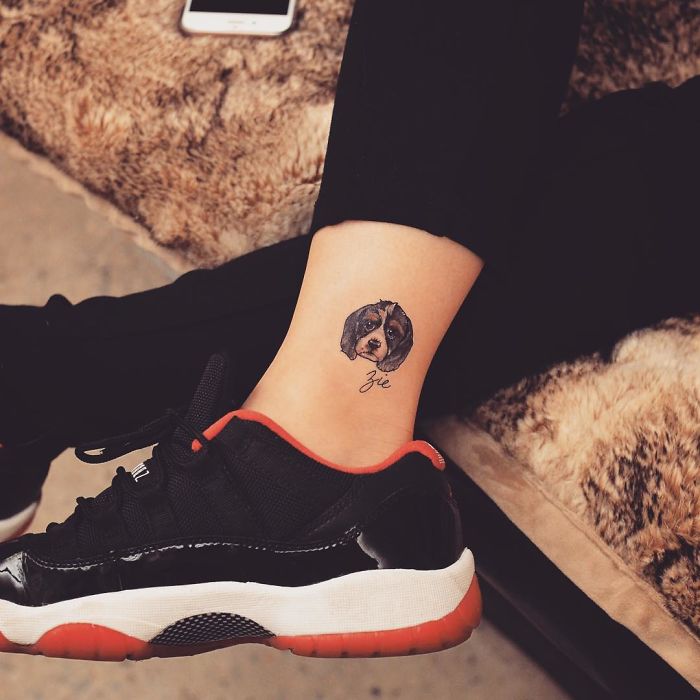 Ankle with a small dog tattoo and name, next to black sneaker.